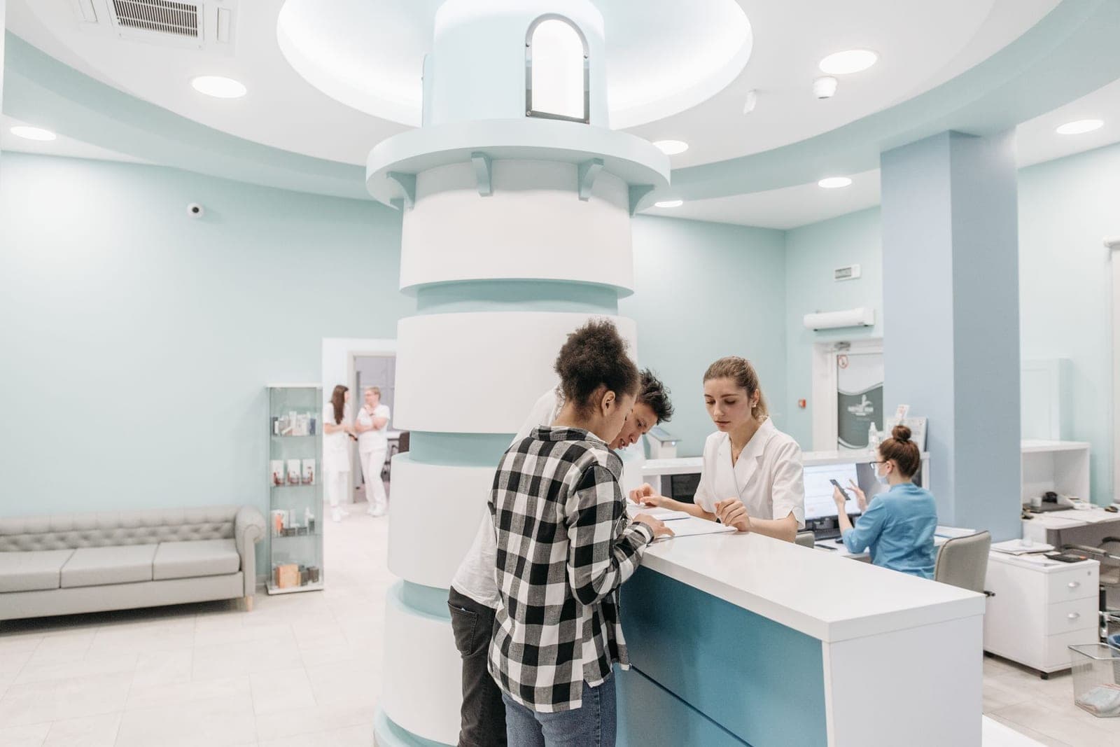 A receptionist at a modern clinic front desk welcoming a patient